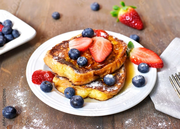 Fototapeta Delicious french toast with fresh fruits and maple sirup. Tasty breakfast scene or dessert with toast, strawberries, blueberries and powdered sugar.