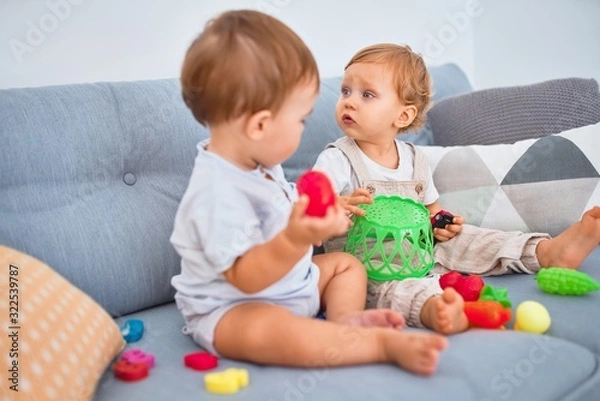 Fototapeta Beautiful toddlers sitting on the sofa playing with toys at home