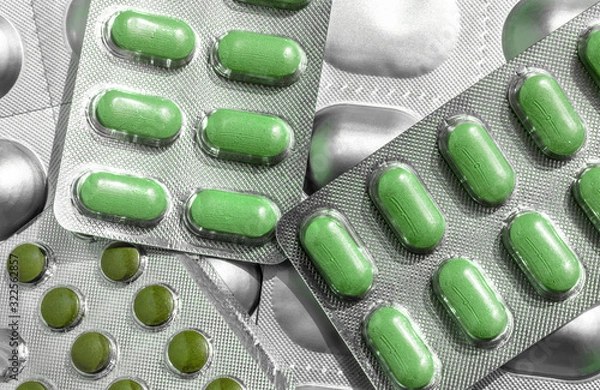Fototapeta Several of blisters with colored green tablets of different shapes close-up