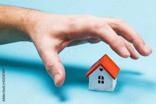 Fototapeta A hand reaches for a toy house. The concept of fraud and theft