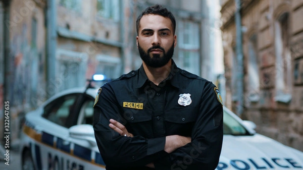 Obraz Close up serious young man cops hold pistol stand near patrol car look at camera enforcement officer police uniform auto safety security communication control policeman portrait slow motion