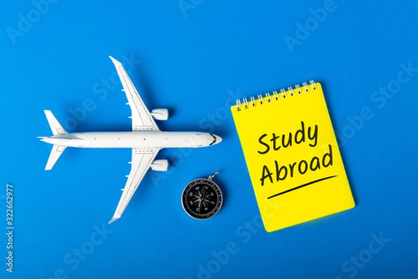 Fototapeta STUDY ABROAD - message on blue background with airplane model. Learning a language and studying abroad
