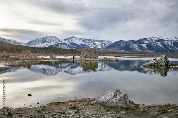 Obraz View of a Saline Soda Lake with Snow Capped Eastern Sierra Navada Mountains on a Cloudy Day in the Afternoon with Sunlight Shinning Through the Cloud 