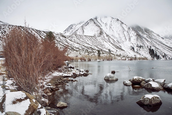 Obraz View of Lake on the Mountains in Winter Fog with Dramatic Snow Capped Mountains in the Background 