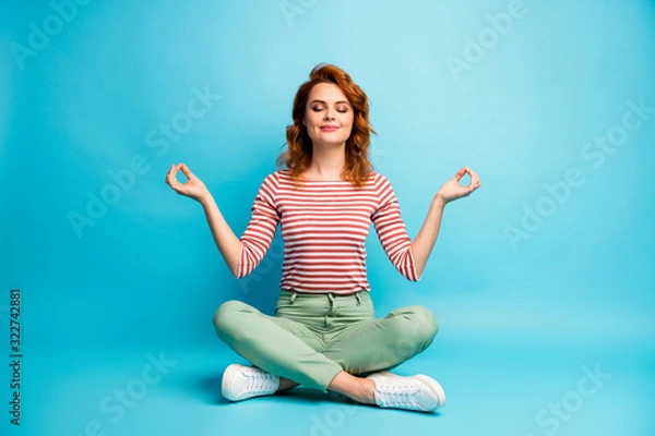 Obraz Pełnowymiarowe zdjęcie cichej, pogodnej kobiety siedzącej na podłodze ze skrzyżowanymi nogami pokaż znak om ćwiczenia joga medytacja nosić stylowy zielony strój odizolowany na niebieskim tle