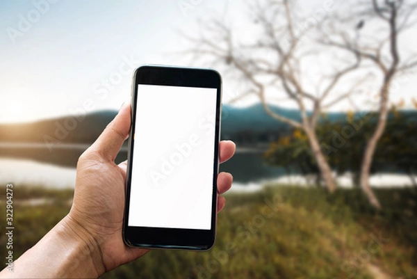 Fototapeta A man hand holding smart phone device in the mountains and blurred background of trees in the forestt