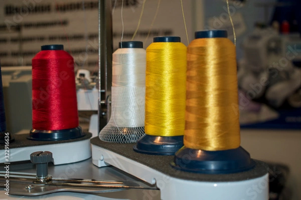 Fototapeta Spools of thread in working condition on sewing equipment. Color is yellow, white, red. Manufactory concept.