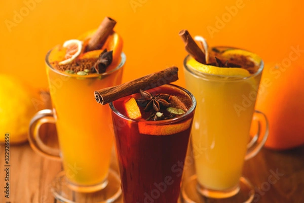 Obraz Three glasses of hot red mulled wine with fruit and spices on wooden table on colorful orange background. Copy space.