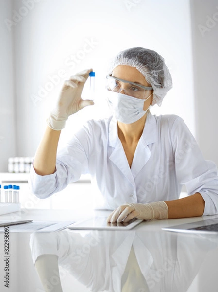 Fototapeta Professional female scientist in protective eyeglasses researching tube with reagents in laboratory. Concepts of medicine and research