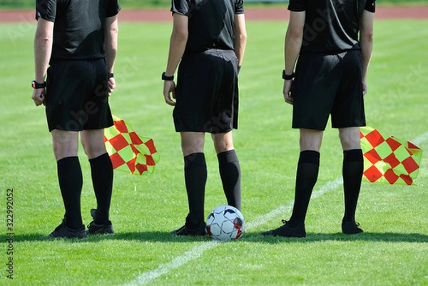 Fototapeta three football referees with flags and a ball before the match