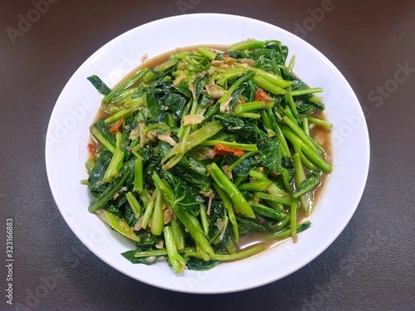 Obraz Top view of stir fried chinese kale mixed spotted mackerel in white plate on wooden table in restaurant, Healthy food concept, Ready to eat or serve