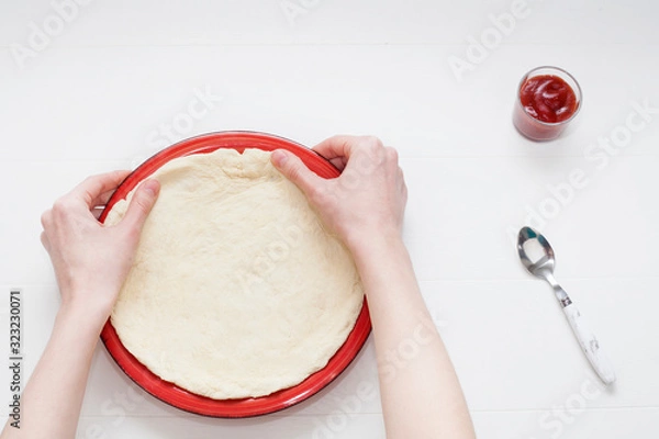 Fototapeta The process of cooking pizza at the stage of rolling out the dough and spread with ketchup, on a white background. The concept of making pizza.