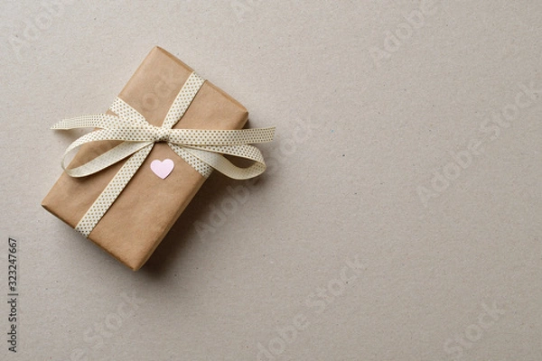 Fototapeta Handmade gift box with a heart, tied with a beige ribbon with a bow, on a cardboard box with space for text.