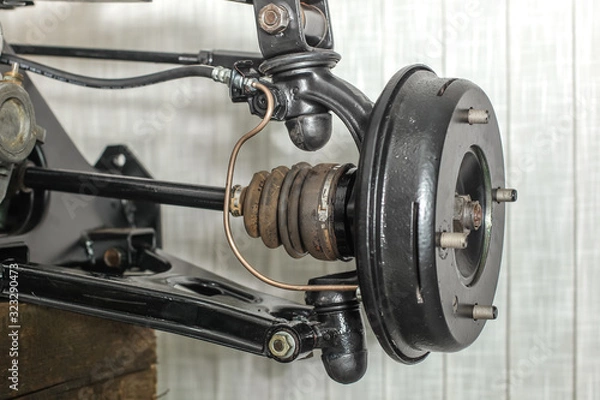 Obraz Front suspension members of an older car with new brake drum exposed with spindle, ball joints and steering rack visible.