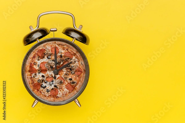Fototapeta Black alarm clock with a pizza instead of a dial. Yellow background.