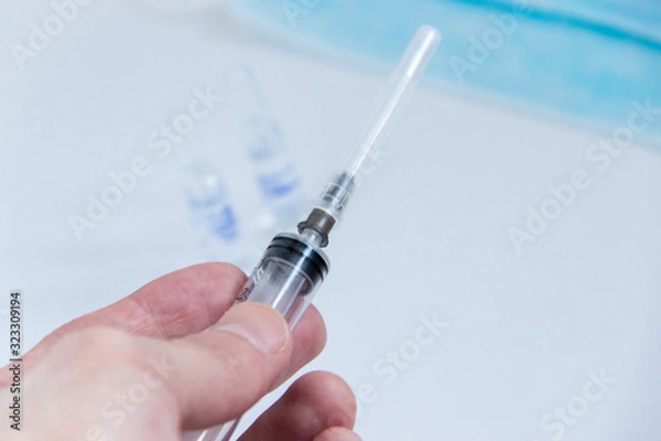 Fototapeta syringe with needle covered in mans hand close up image.