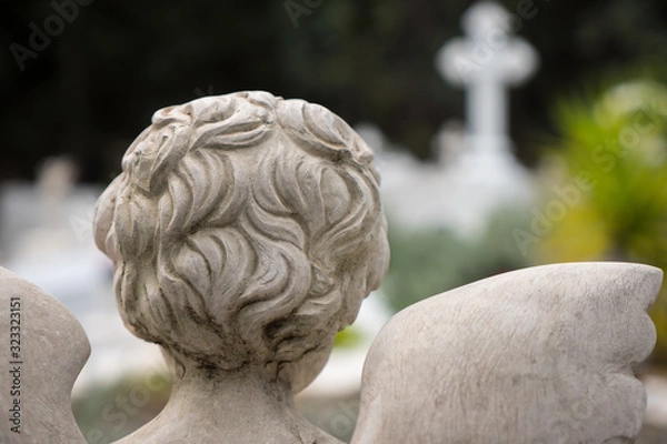 Fototapeta Back view of an Angel looking towards a marble cross in a graveyard