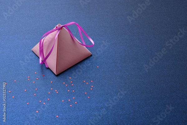 Fototapeta Festive background for Valentine's Day, International women's day, Christmas and New year. Holiday card, with a pink pyramidal gift box on a blue silver background with red stars, space for text.