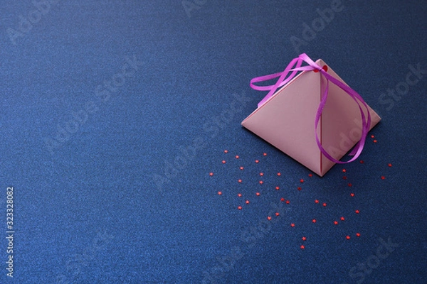 Fototapeta Holiday card, with a pink pyramidal gift box on a blue silver background with red stars, space for text. Festive background for Valentine's Day, International women's day, Christmas and New year. 