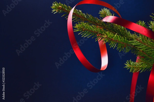 Fototapeta Spruce branch with a red ribbon on a dark blue background and space for text.