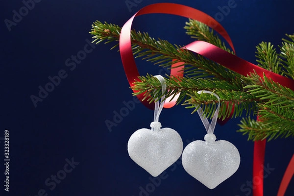Fototapeta Still life for Valentine's day two silver hearts on a coniferous branch with a red ribbon on a dark blue background, space for text.
