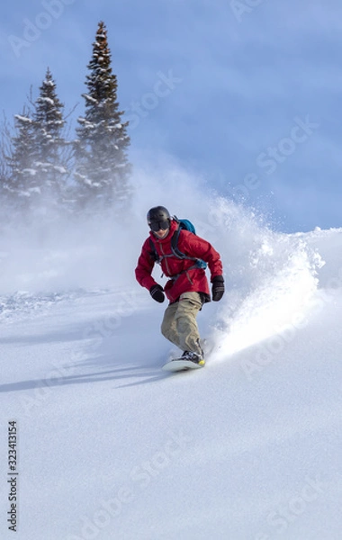 Obraz heliski snowboarding. freerider in a bright suit rides snowboarding with large splashes of snow on a sunny day. Young snowboarder. concept snowboard. big swirls of fresh snow in Good powder day