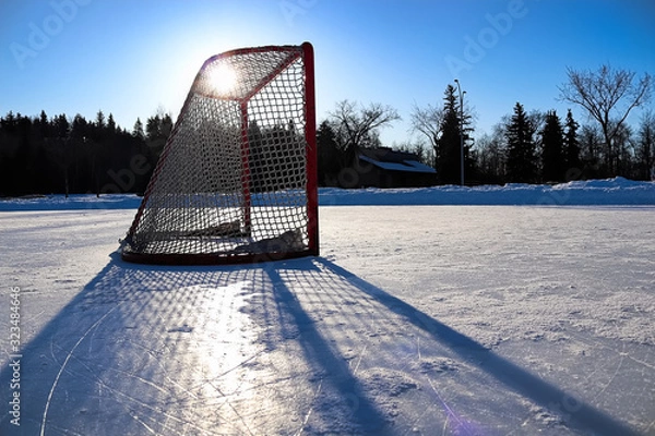 Fototapeta Sun silhouetting a empty hockey net on a frozen pond