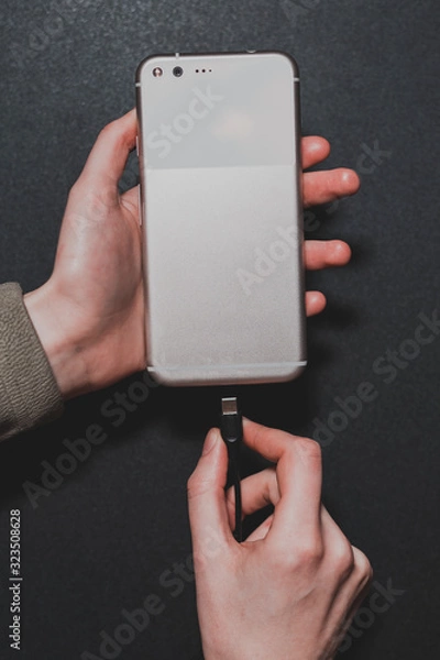 Fototapeta close-up of female hands that plug a smartphone into charging on a black background