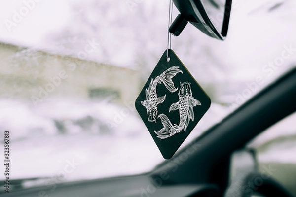 Fototapeta freshener in the car in the form of a drawing of the zodiac sign of a fish on a black square on the background of a snow-covered windshield.