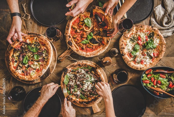 Fototapeta Rodzina lub przyjaciele jedzą kolację z pizzą. Płaski leżak ludzi biorących i jedzących różne rodzaje pizzy i popijających czerwone wino przy rustykalnym drewnianym stole, widok z góry. Obiad typu fast food, świętowanie