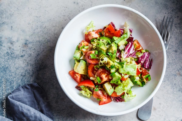 Fototapeta Avocado and tomato salad in white bowl, top view. Vegan food concept.