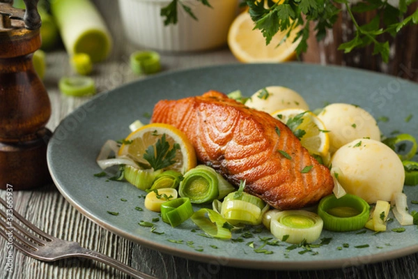 Fototapeta Portion of fried salmon, served with mashed potatoes and cooked leek. Front view. Gray plate, wooden background.