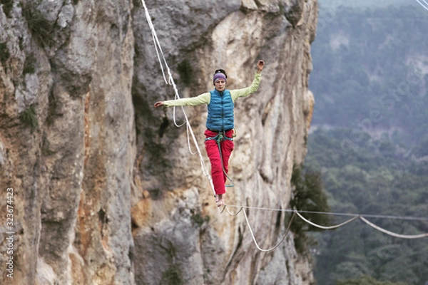 Obraz A woman is walking along a stretched sling. Highline in the mountains. Woman catches balance. Performance of a tightrope walker in nature.