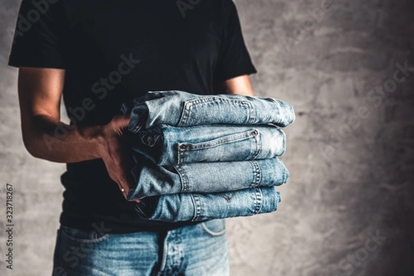 Fototapeta close up stack of folded denim blue jeans in hand over gray wall background, copy space