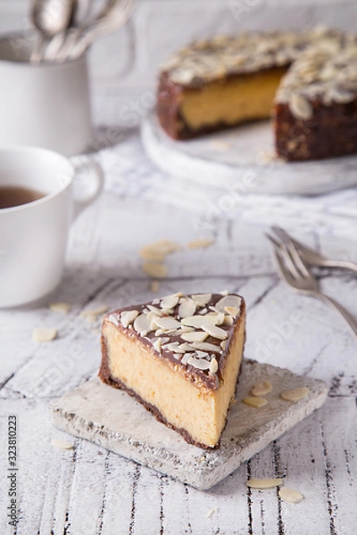 Fototapeta Piece Slice of Сheesecake with Chocolate, Caramel, Peanut Paste, Nougat Layered Cake on white table background