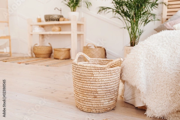 Fototapeta Light interior made of natural ecoy components. Wicker straw basket for storing clothes and things on the background of the washbasin and bath in the Boho style with wicker baskets and wooden shelves