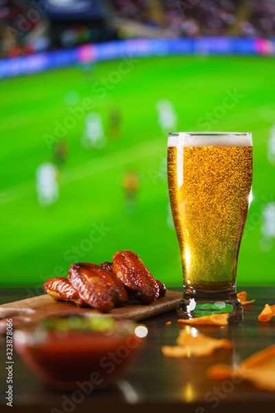 Fototapeta Spicy barbecue chicken wings, tomato salsa, nachos and beer on dark wooden bar table. Football on background, high resolution