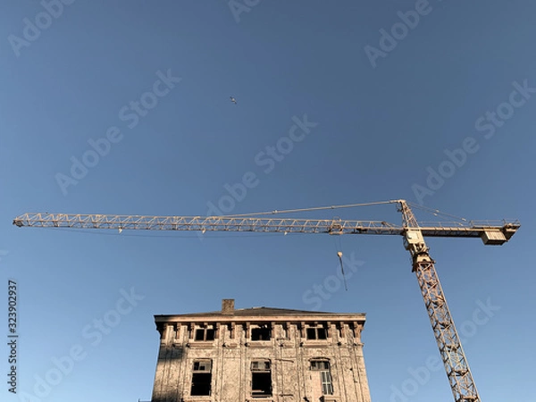 Fototapeta Yellow construction crane and reconstruction of old buildings, blue sky background