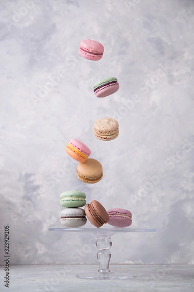 Fototapeta Sweet french macaroons falling in motion on grey background. Pastel colored flying macaroons cookies. Food, culinary and cooking concept