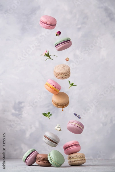Fototapeta Sweet macaroons cookies falling in motion on grey background. Pastel colored flying macaroons with ingridients. Food, culinary and cooking concept levitation