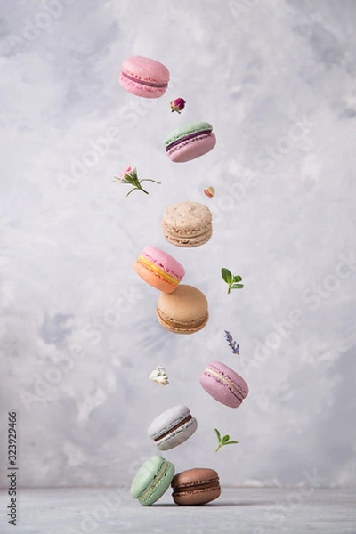 Fototapeta Sweet macaroons cookies falling in motion on grey background. Pastel colored flying macaroons with ingridients. Food, culinary and cooking concept levitation