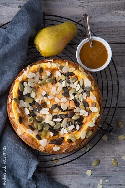 Fototapeta Autumn pear pie with pumpkin seeds and almond petals on blue grey wooden table with caramel, top view
