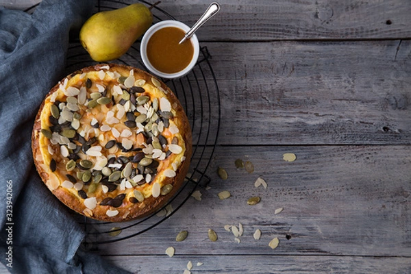 Fototapeta Autumn pear pie with pumpkin seeds and almond petals on blue grey wooden table with caramel, top view