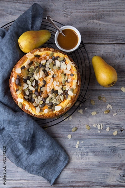 Fototapeta Autumn pear pie with pumpkin seeds and almond petals on blue grey wooden table with caramel, top view