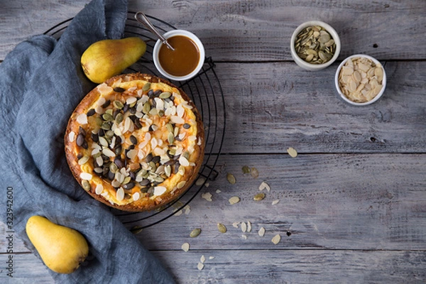 Fototapeta Autumn pear pie with pumpkin seeds and almond petals on blue grey wooden table with caramel, top view