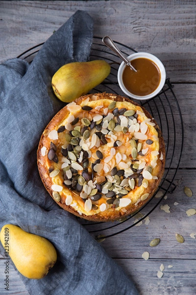 Fototapeta Autumn pear pie with pumpkin seeds and almond petals on blue grey wooden table with caramel, top view