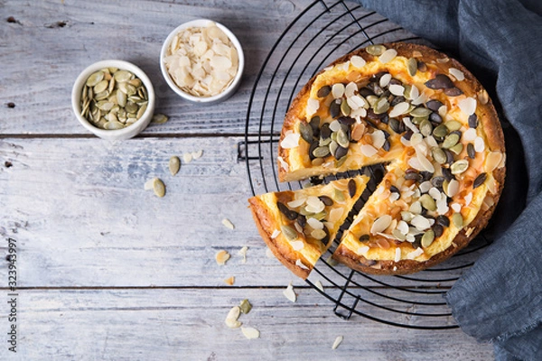 Fototapeta Pears and cheese pie with bowl of caramel, pumpkin seeds and almond petals. Top view. Copy space flat lay