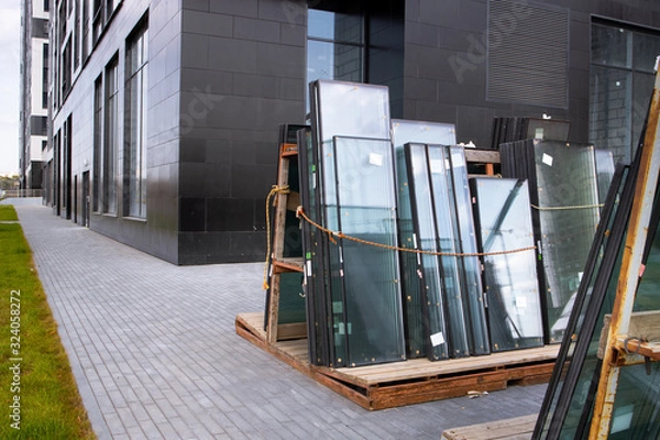 Fototapeta Installation of windows in a house under construction. New residential buildings. New Apartments for settlement. Crane builds a house on a background of blue sky. Urbanization. ..