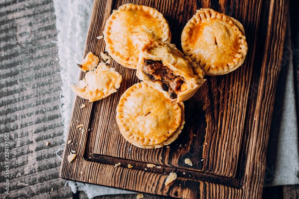 Fototapeta Fresh Traditional Australian meat mini pie on the wooden board on table background, closeup with copy space, rustic style