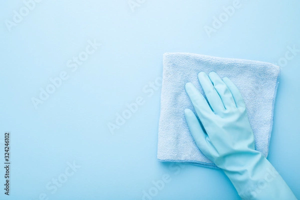Fototapeta Hand in rubber protective glove wiping table, wall or floor surface in kitchen, bathroom or other room. Closeup. Empty place for text or logo. Light pastel blue background. Top down view.